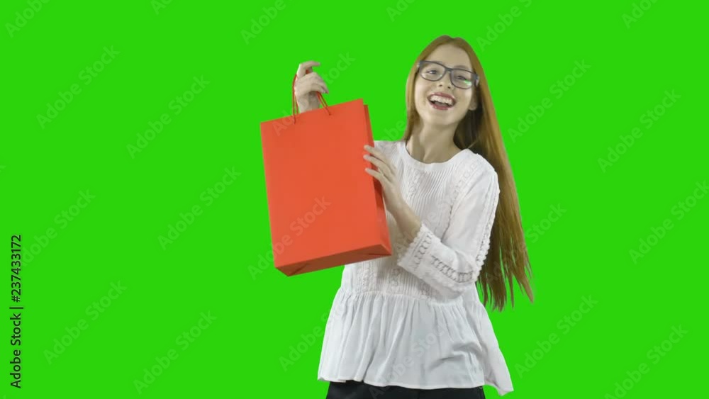 Happy and joyful girl with a red paper bag after shopping in a mall on an isolated green background. Happy and joyful girl with a red paper bag after shopping in a mall on an isolated green background.