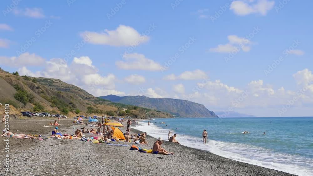 September 6, 2018, Morskoye village, Crimea, editorial. People in bathing suits on a pebble beach by the sea. Mountains against the blue sky with white clouds. Cirrus clouds run across the blue sky September 6, 2018, Morskoye village, Crimea, editorial. People in bathing suits on a pebble beach by the sea. Mountains against the blue sky with white clouds. Cirrus clouds run across the blue sky
