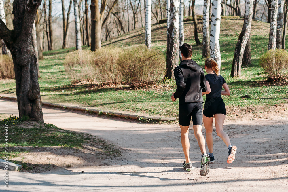 Fototapeta premium man and young woman athlete in sportswear summer early morning running in Park. healthy lifestyle concept. rear view