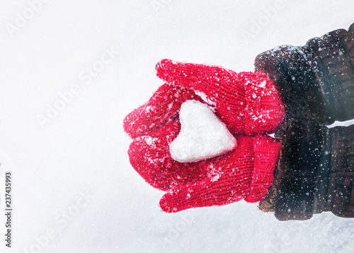 Female hands in knitted mittens with heart of snow in winter day. Love concept. Valentine day background.