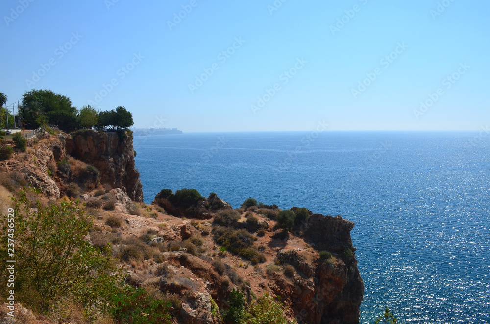 Blue Mediterranean Sea with a steep coast on a sunny day. City on the horizon.