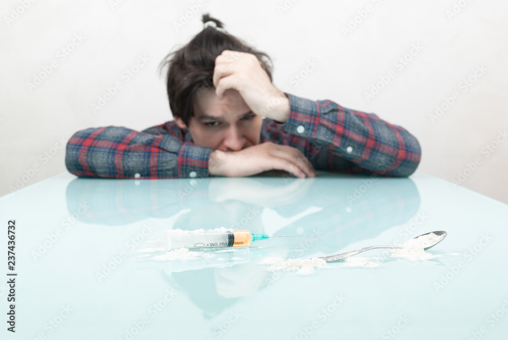 young guy looks at a syringe with heroin young guy looks at a syringe with heroin