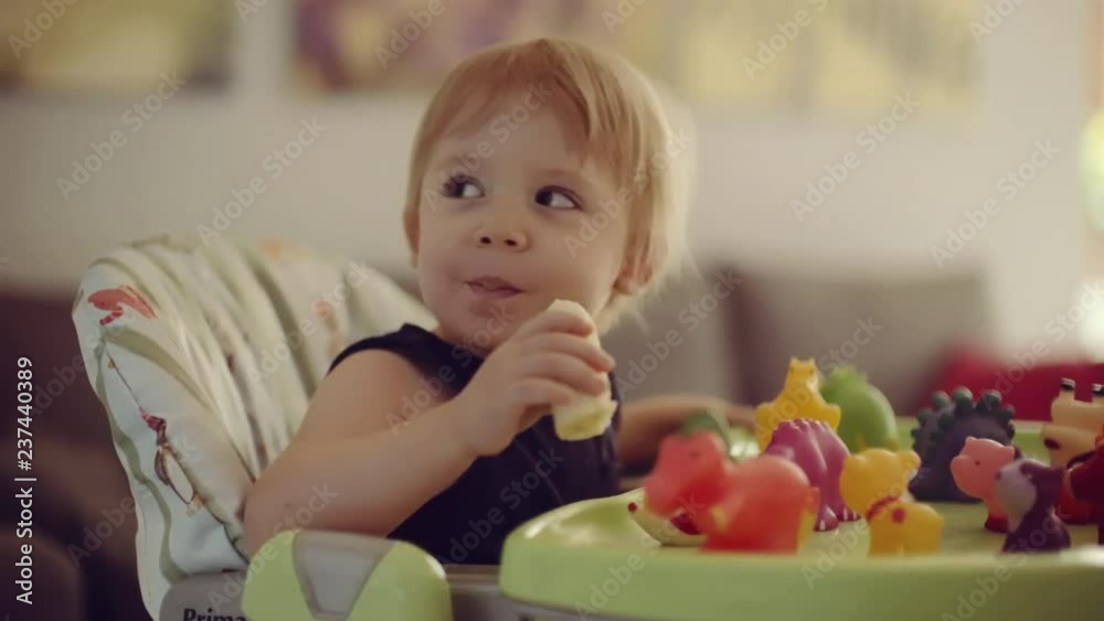 little boy sitting on high chair eating banana little boy sitting on high chair eating banana