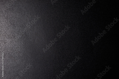 Black, rough textured background lit with dim light.