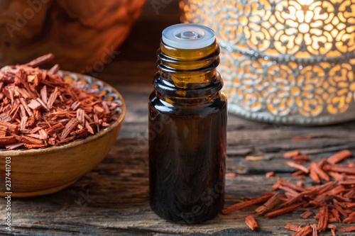 A bottle of sandalwood essential oil with pieces of red sandalwood photo