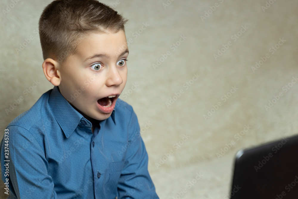 A child with a very surprised face, sitting in front of a laptop screen. A boy with an open mouth and bulging eyes in front of a computer. A child with a very surprised face, sitting in front of a laptop screen. A boy with an open mouth and bulging eyes in front of a computer.