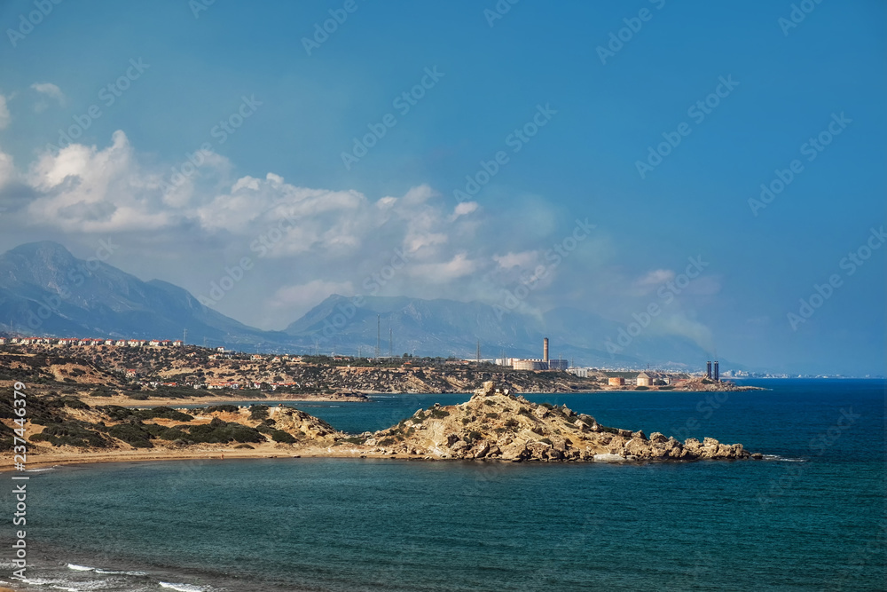 Desert coastline with sand Alagadi beach of Northern Cyprus and factory and mountains on horizon