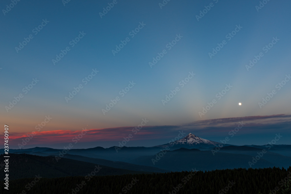 Obraz premium the last rays of sunshine streak through the sky with the full moon sitting over a mountain