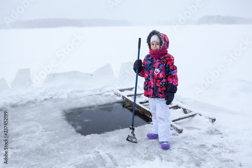 Young girl with axe in hand for ice cutting is standing near ice-hole at lake photo