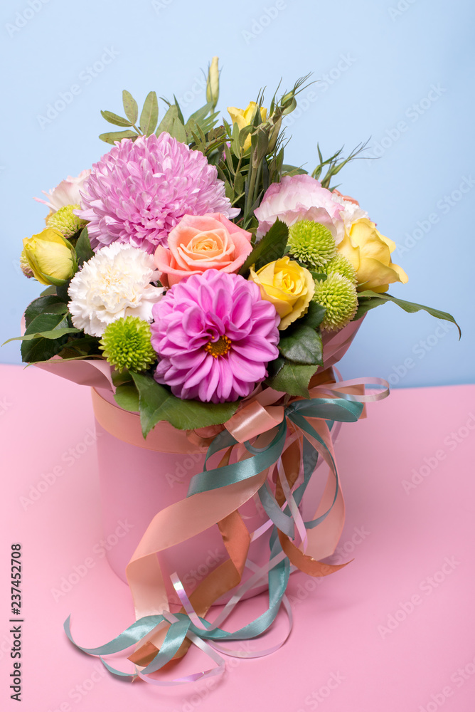 Naklejka premium beautiful floral arrangement in the box, pink and yellow rose, pink eustoma, green and pink chrysanthemum, white carnation, pink dahlia on pink, blue background with space for text.