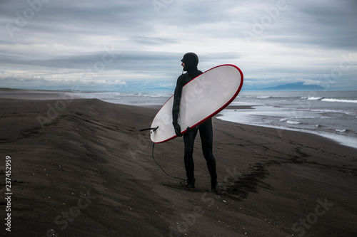 Surfing on the black volcanic beach of the Pacific Ocean, Kamchatka, Russia, the Far East. Extreme sport in cold water.