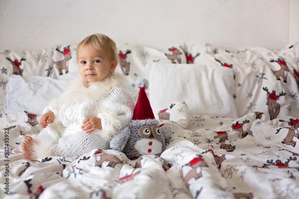 Adorable little baby boy in handknitted overall, eating cookies in bed on Christmas