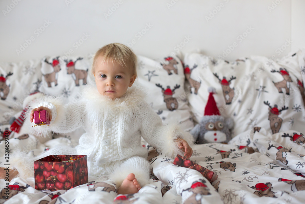 Adorable little baby boy in handknitted overall, eating cookies in bed on Christmas