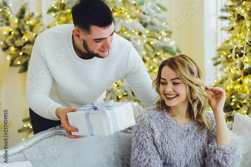 The guy gives a gift to the girl on the background of the Christmas tree. Christmas background