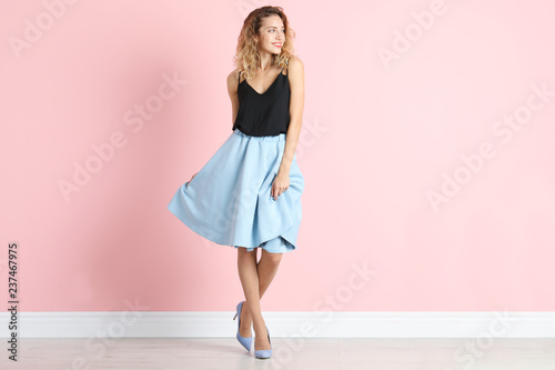 Young woman with beautiful long legs in stylish outfit near color wall