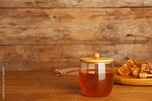 Glass jar with sweet honey on table against wooden background. Space for text