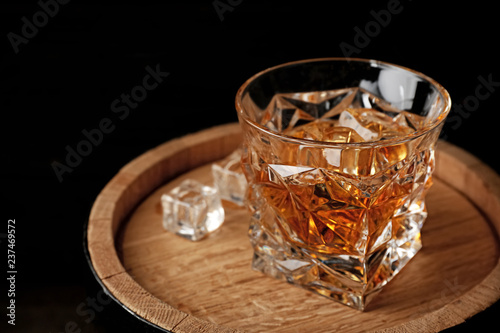 Golden whiskey in glass with ice cubes on wooden barrel. Space for text