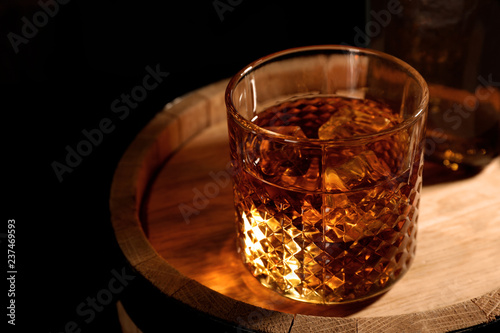 Golden whiskey in glass with ice cubes on wooden barrel. Space for text