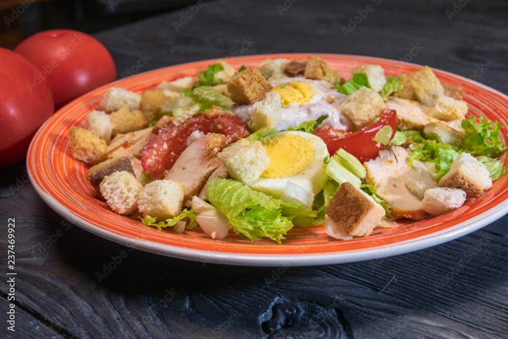 Caesar salad in red plate. Caesar salad consists of roasted chicken breast, iceberg lettuce, tomato, parmesan cheese. Popular dish of European cuisine and cuisines of other countries. Caesar salad in red plate. Caesar salad consists of roasted chicken breast, iceberg lettuce, tomato, parmesan cheese. Popular dish of European cuisine and cuisines of other countries.