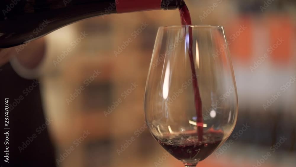 Slow pouring red wine into a wine glass. Female hand pours wine into a wine glass close up.