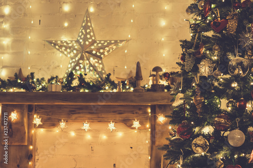 Beautiful decorated wood mantelpiece, lit up Christmas tree with baubles and ornaments, wooden decorations, silver star, icicle lights, toned, selective focus