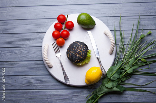 Black wooden serving tray with black burger, potato wedges and ketchup, vertical shot on a grey stone background photo