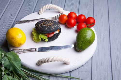 Black wooden serving tray with black burger, potato wedges and ketchup, vertical shot on a grey stone background photo