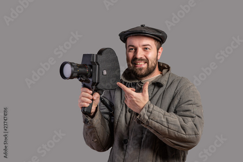 Concept - please smile. Emotional cameraman with retro camera in his hands, studio shot. Old-fashioned clothing style. Movie of the 70th
