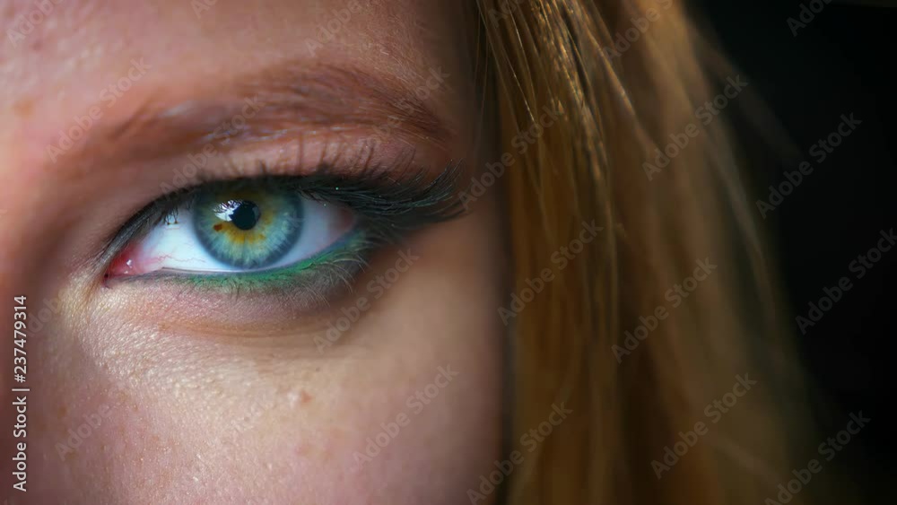 Amazing green and blue eyeshadows close up on caucasian girls eye close up looking relaxed and showing her be fashionable cosmetics indoors, dark background Amazing green and blue eyeshadows close up on caucasian girls eye close up looking relaxed and showing her be fashionable cosmetics indoors, dark background