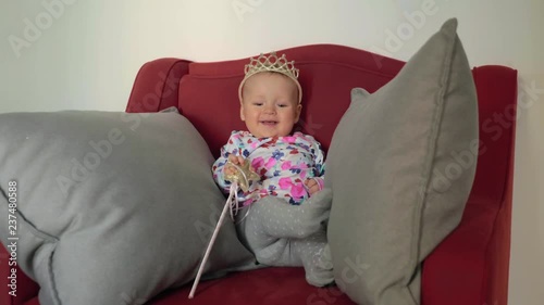 Medium shot of a baby girl wearing a princess crown and holding a wand on a red chair photo