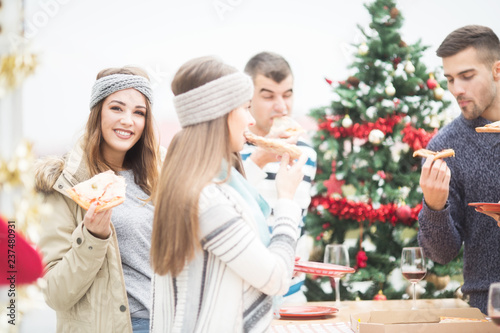 Young woman eating Pizza with friends on balcony for Christmas