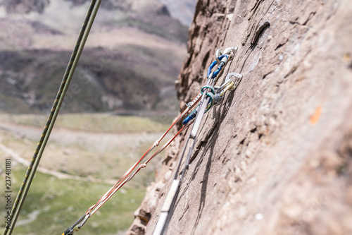 Rock climbing belay station in the middle of an Andes mountain rock face. Ropes, belaying devices, bolts, carabiners all making a triangle of forces to reduce the forces around the bolts