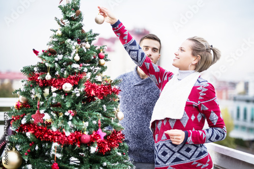 Young couple decorating Christmas tree on balcony
