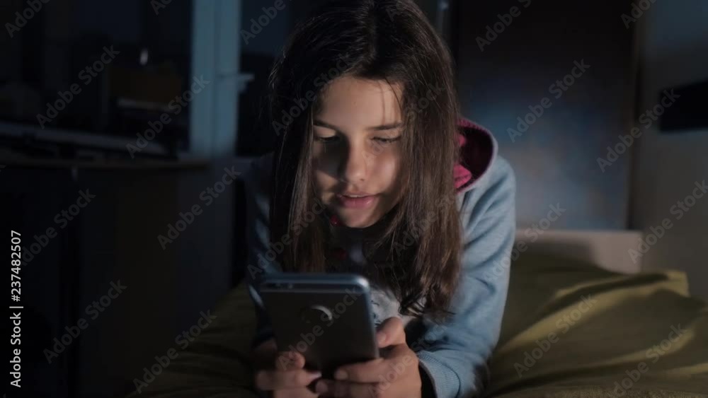 girl teenager and smartphone. little teen hood girl writes a message chatting in social media messenger night evening indoors smartphone on the bed. children technology and communication concept girl teenager and smartphone. little teen hood girl writes a message chatting in social media messenger night evening indoors smartphone on the bed. children technology and communication concept