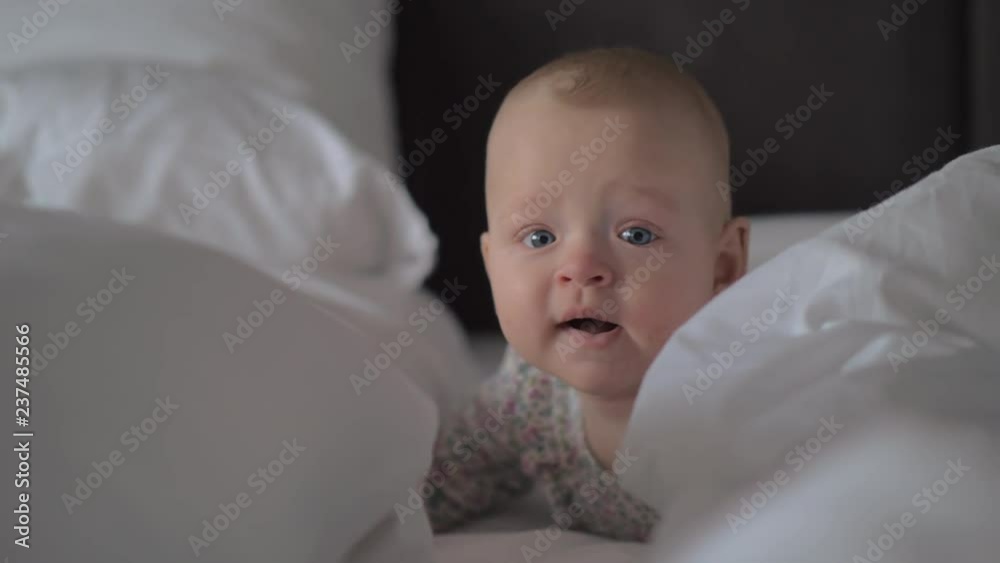 A closeup of a cute baby girl with bright grey eyes, lying on her tummy on white sheets. She is looking around, putting her head down from time to time A closeup of a cute baby girl with bright grey eyes, lying on her tummy on white sheets. She is looking around, putting her head down from time to time