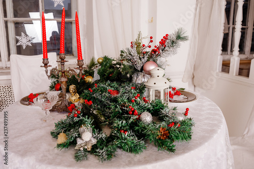 Fototapeta Naklejka Na Ścianę i Meble -  Christmas Family Dinner Table Concept.Table setting for new year dinner.decorations, candles and lanterns. white tablecloth. Living room decorated with lights and Christmas tree. Holiday setting
