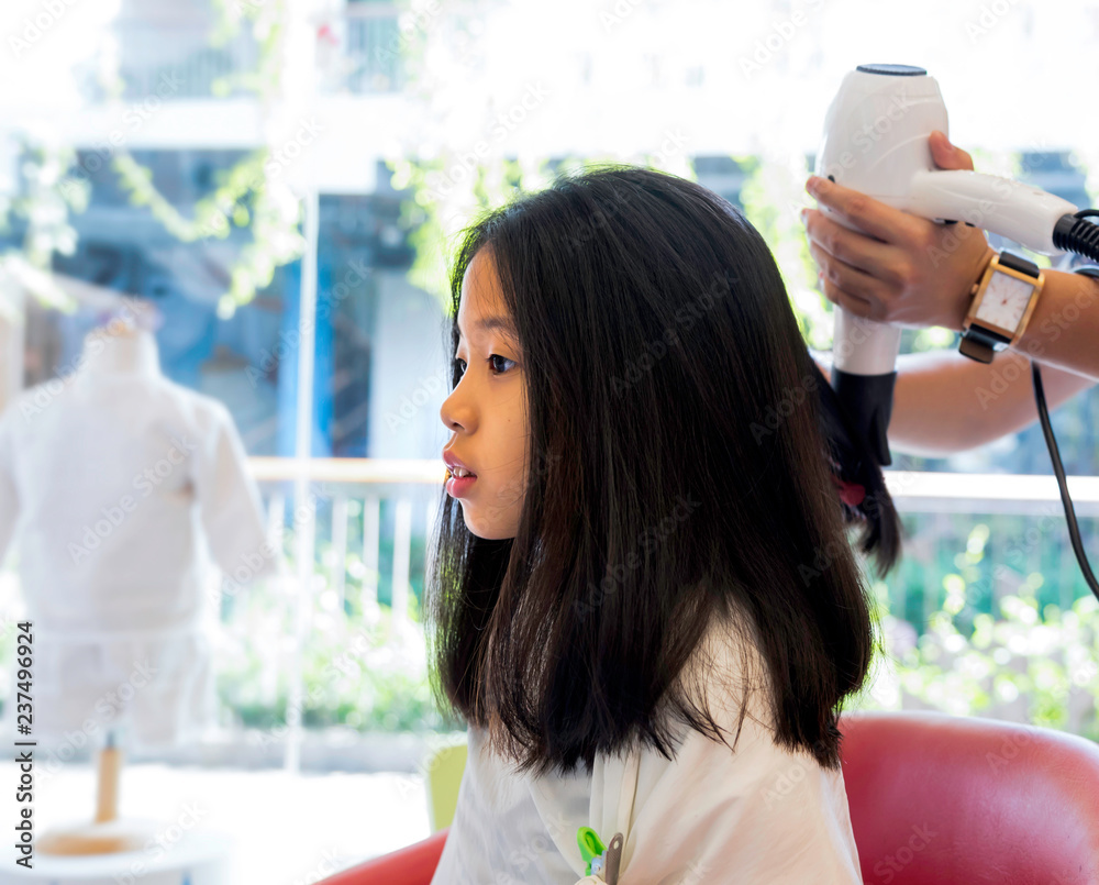 Portrait of Asian kid with healthy long black hair getting haircut. Hand of  stylist drying woman