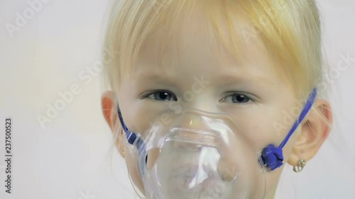 Close-up of a four-year-old girl doing breathing procedures through an inhaler mask in a hospital.