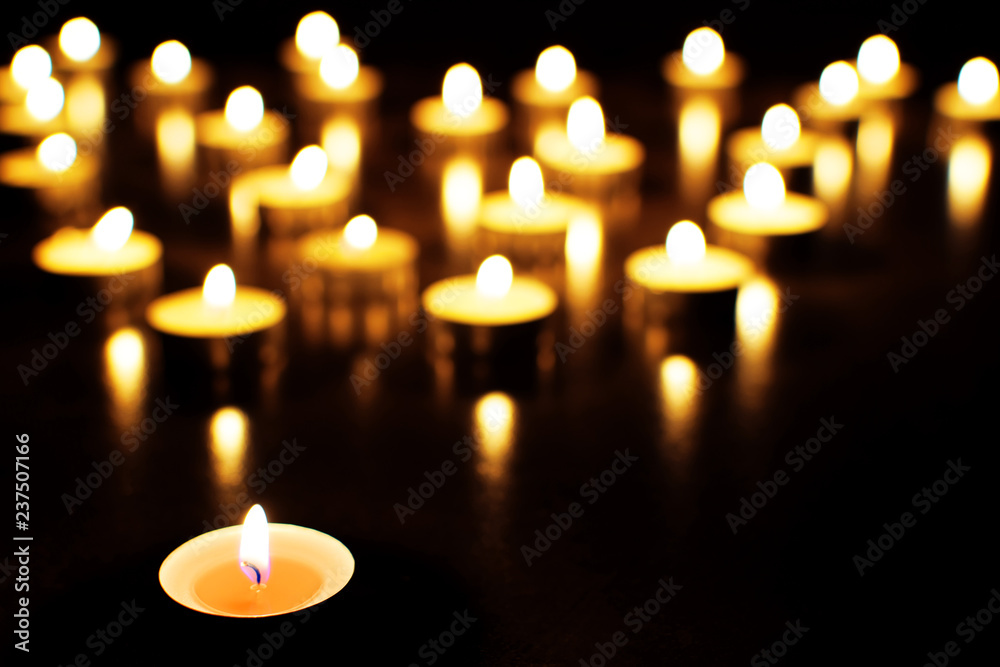 Yellow tea light candles burning in darkness. Advent or memorial prayer candle flame.