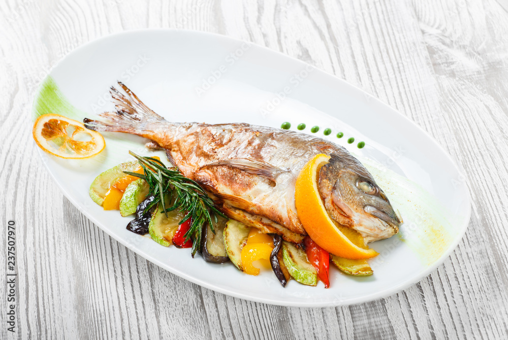 Grilled dorado fish with baked vegetables and rosemary on plate on wooden background close up. Healthy food. Top view Grilled dorado fish with baked vegetables and rosemary on plate on wooden background close up. Healthy food. Top view