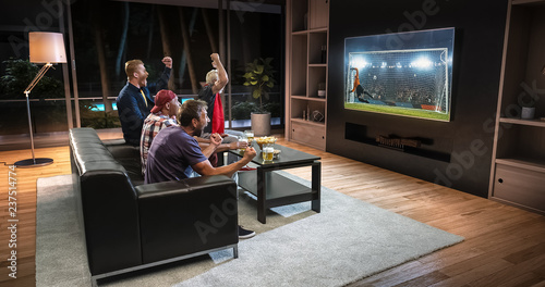 Group of fans are watching a soccer moment on the TV and celebrating a goal  sitting on the couch in the living room.