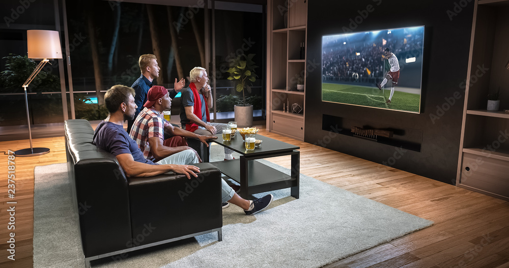 Group of fans are watching a soccer moment on the TV and celebrating a goal, sitting on the couch in the living room. Group of fans are watching a soccer moment on the TV and celebrating a goal, sitting on the couch in the living room.