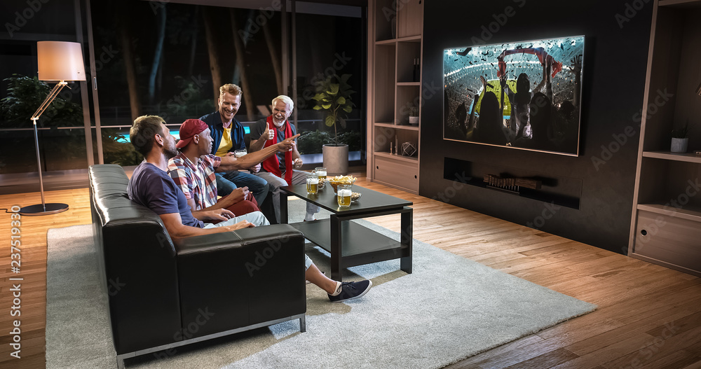 Group of fans are watching a soccer moment on the TV and celebrating a goal, sitting on the couch in the living room. Group of fans are watching a soccer moment on the TV and celebrating a goal, sitting on the couch in the living room.