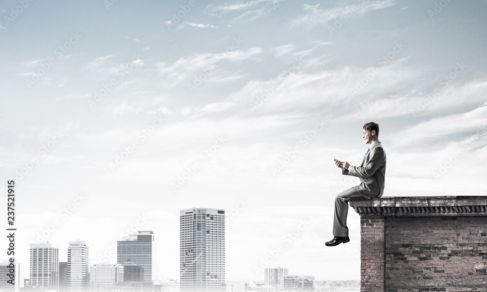 Man on roof edge send message with smartphone and cityscape at b