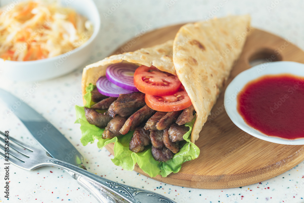 Handmade doner kebab is lying on the white table made of artificial stone Shawarma on the wooden cutting board with chicken meat, onions, salad lies on a dark old wooden table. Handmade doner kebab is lying on the white table made of artificial stone Shawarma on the wooden cutting board with chicken meat, onions, salad lies on a dark old wooden table.