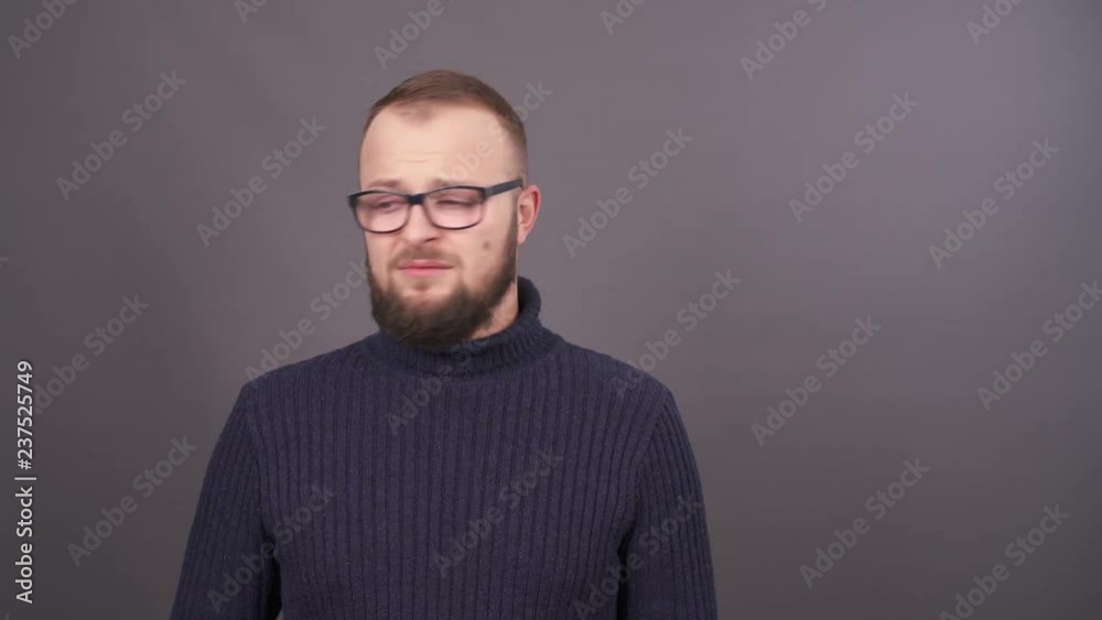 Close-up portrait of young bearded caucasian man in glasses felling confused and embarrassed. Isolated on grey background.