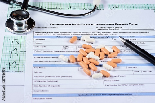 Prescription drugs prior authorization request form, pills, stethoscope and pen on a EKG graph paper background. Close-up.