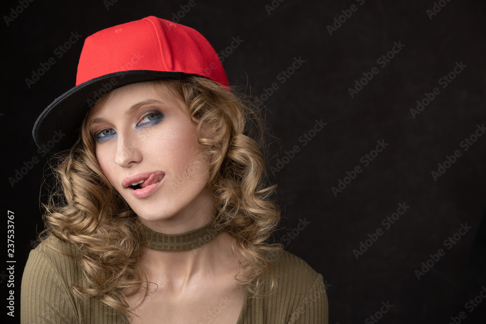 Portrait of naughty girl in red cap and with tongue. Space for text and copy-paste. Dark Studio background and a vivid portrait of the model Portrait of naughty girl in red cap and with tongue. Space for text and copy-paste. Dark Studio background and a vivid portrait of the model