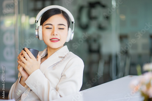 A beautiful Asian woman close her eyes and listening to music with headphone while drinking coffee with feeling happy and relax.