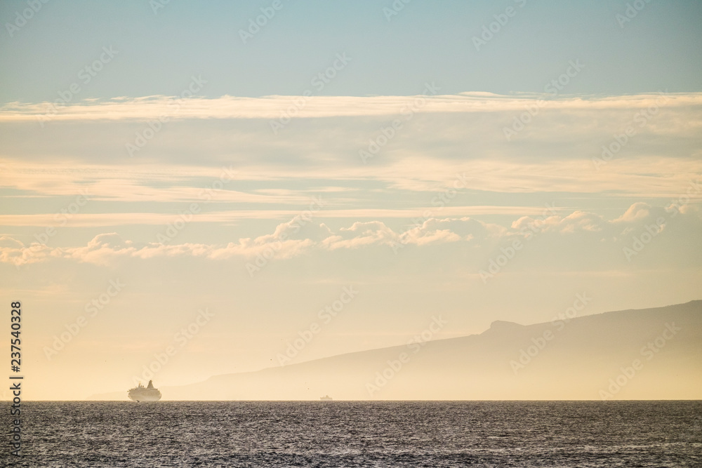 Travel and vacation concept with two cruise boat on the line horizon during a beautiful sunset weather near a tropical island in the ocean - people traveling concept